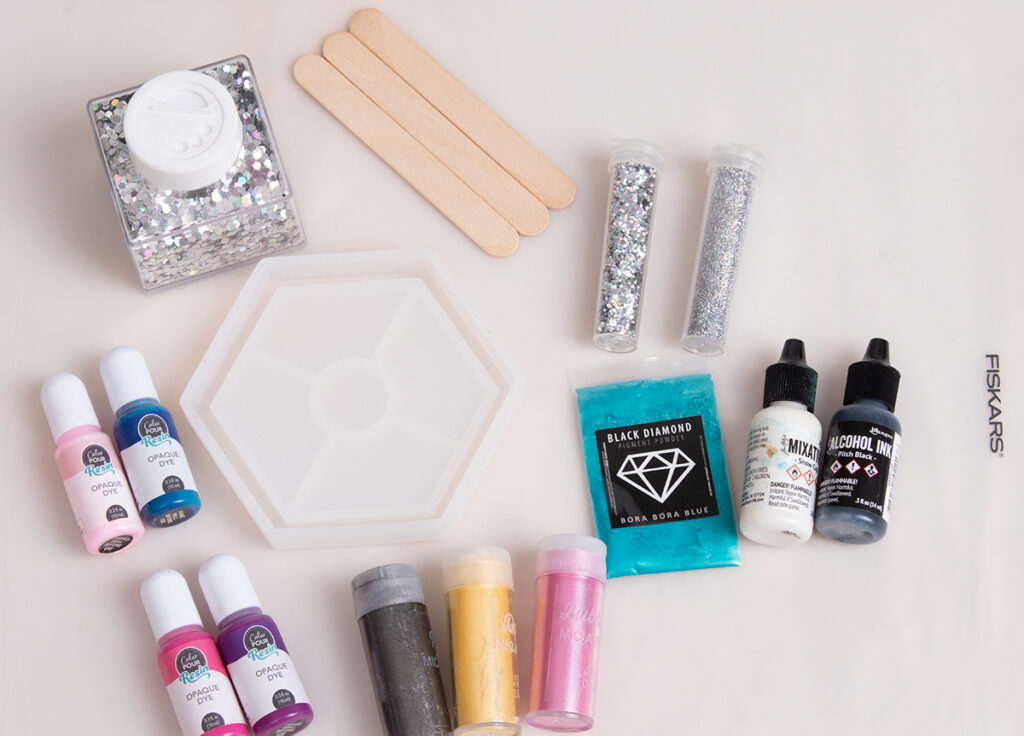 Hexagon-shaped, silicone coaster mold, popsicle sticks, opaque dyes, mica powders, alcohol inks, and holographic glitters.