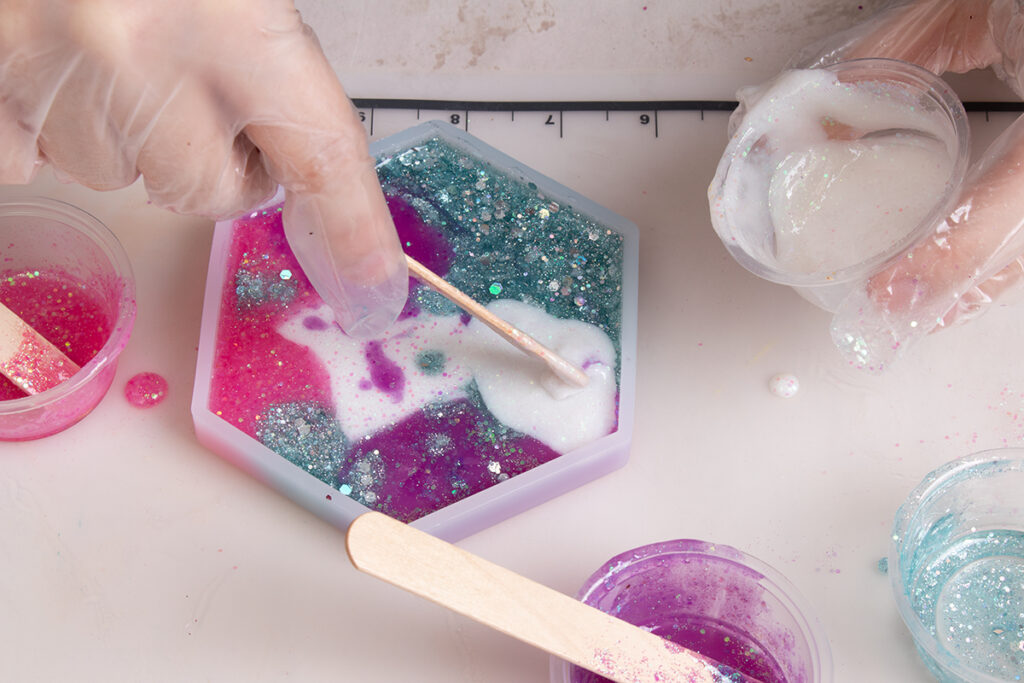 Adding more white glitter resin with a popsicle stick to coaster mold to fill in empty spots