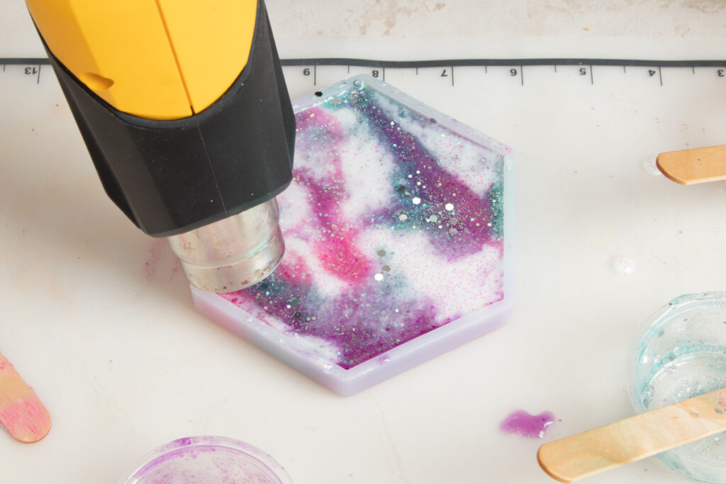 Heat gun pointed over full silicone mold to pop bubbles and mix around the colors.